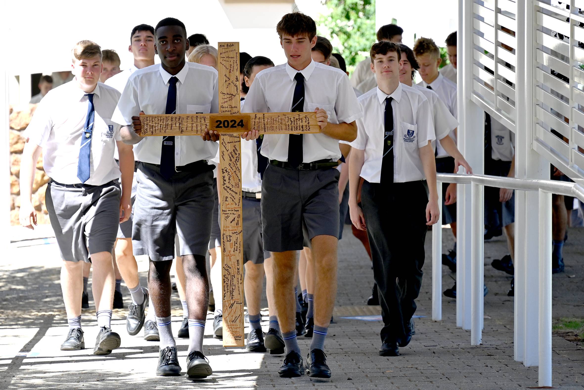 A photo of year 12 students walking with the cross that they all sligned.